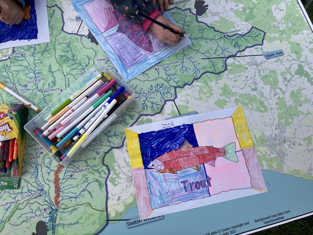 A table with a map, colourful picture of a trout and a child's hand colouring in.