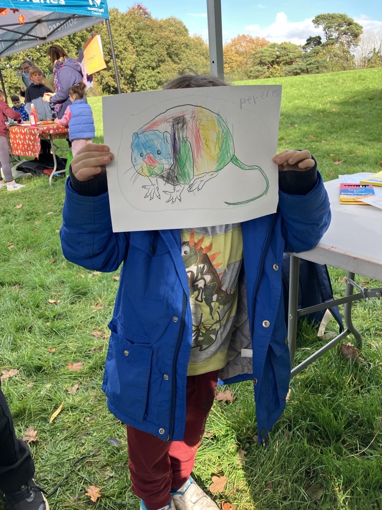 A child holding up a coloured-in picture of a water vole